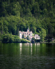 A picturesque historic villa resembling a fairytale castle stands nestled among dense green forest...