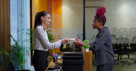 Happy young adult gen z woman lady staff agent standing at desk table do help check in give key...