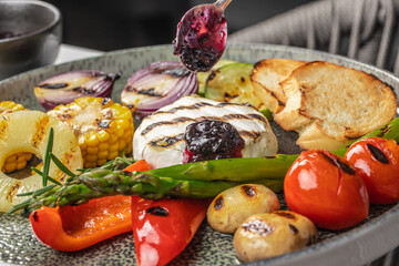 A colorful grilled vegetable platter with creamy baked Camembert cheese, topped with a spoonful of...