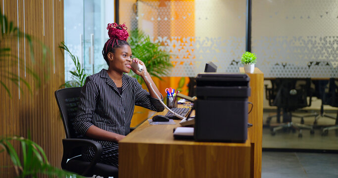 African young adult gen z woman lady sitting chair desk table use computer look screen do work task typing email check data at job office expert staff busy female girl attend phone calls talk day time