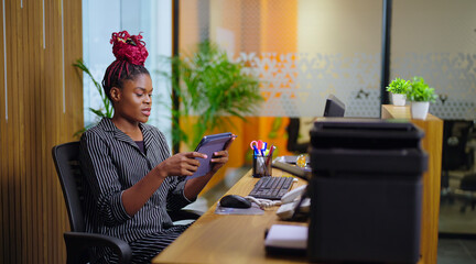 African young adult gen z busy woman lady sitting on chair use tablet device touch screen typing girl female agent hold gadget do work day task check email data read news play game job office place