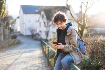 Teen girl using smartphone on town street. Teenager with gadget outdoors. Early spring. School-aged...