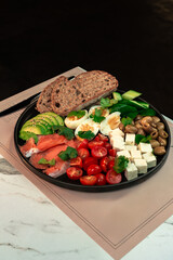 Hearty Smoked Salmon Breakfast Bowl with Avocado, Egg & Feta. Multigrain bread, cherry tomatoes, cucumber and olives plated for a nutritious morning meal.