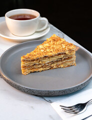 Flaky Napoleon Cake Slice on Plate with Tea. Classic multi layered puff pastry dessert with creamy...