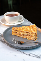 Flaky Napoleon Cake Slice on Plate with Tea. Classic multi layered puff pastry dessert with creamy...