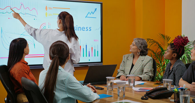 Indian young female old boss lady team leader show chart white board learn study graph data growth serious work place Asian adult girl staff group talk speak share stock trade idea plan job office day