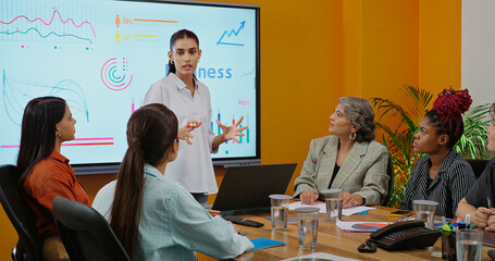 Indian young female old boss lady team leader show chart white board learn study graph data growth serious work place Asian adult girl staff group talk speak share stock trade idea plan job office day