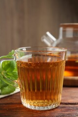 Aromatic lemon balm tea in glass cup, teapot and fresh leaves on wooden table, closeup
