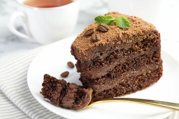 Piece of delicious chocolate cake with coffee beans, mint and fork on light table, closeup