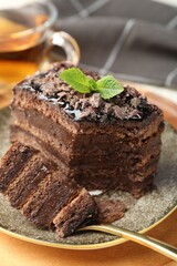 Piece of delicious chocolate cake with mint and tea on table, closeup