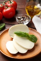 Tasty mozzarella, tomatoes and basil on wooden table, closeup