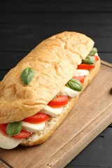 Tasty sandwich with mozzarella cheese, tomatoes and basil on black wooden table, closeup