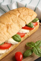 Tasty sandwich with mozzarella cheese, tomatoes and basil on table, closeup