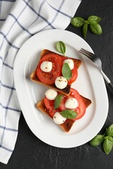 Tasty sandwiches with mozzarella cheese, tomatoes, basil and fork on dark textured table, flat lay