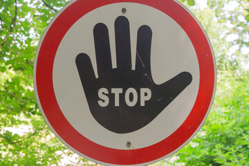 Round stop sign with a black hand symbol on a white background and red border, mounted on a wooden...