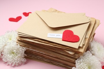 Stack of letters with phrase I Love You, flowers and red hearts on pink background, closeup