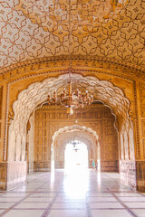 The majestic interior of Badshahi Mosque reveals stunning Mughal arches and intricately patterned ceilings, bathed in soft light, offering a glimpse into historical grandeur and Islamic artistry.