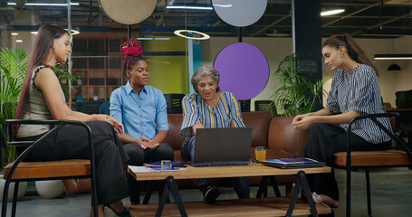 Indian old aged boss lady do work talk speak good news share new deal ideas plan job place happy female girl staff group team sitting on chair sofa couch use laptop look screen at office