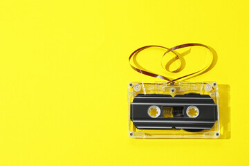 One audio cassette with heart shaped magnetic tape on yellow background, top view. Space for text