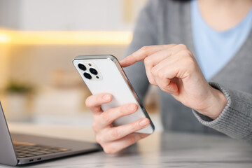 Woman using modern smartphone at white marble table indoors, closeup