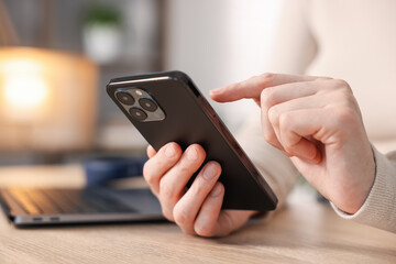 Woman using modern smartphone at wooden table indoors, closeup