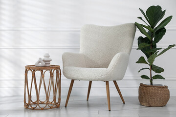 Comfortable armchair, side table and houseplant near white wall indoors