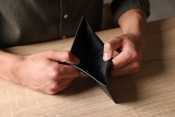 Man with empty wallet at wooden table, closeup