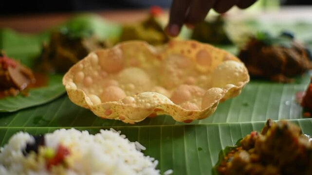 crisp, freshly made pappadam being served onto banana leaf laden with colorful onam sadya dishes. rice, curries in background. concept of indian food, kerala tradition.food, culinary arts