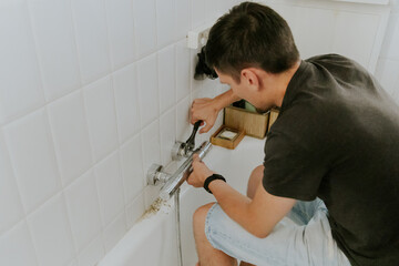 A young man installs a faucet in the bathroom.
