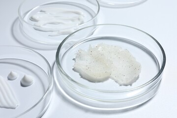 Different cosmetic products in Petri dishes on white background, closeup