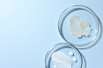 Different cosmetic products in Petri dishes on light blue background, flat lay. Space for text