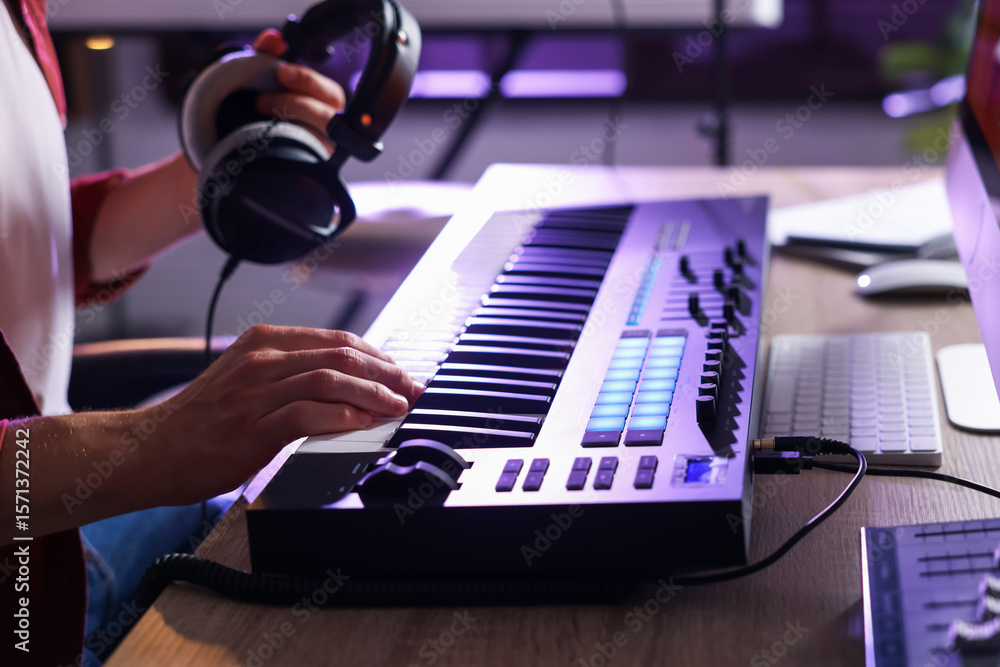 Poster man with headphones working with midi keyboard at table indoors, closeup