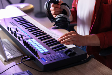 Man with headphones working with MIDI keyboard at table indoors, closeup