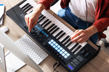 Man working with MIDI keyboard at wooden table indoors, above view