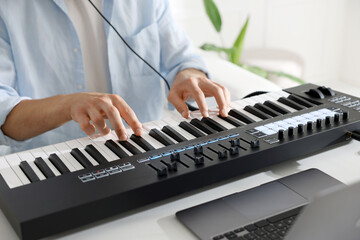Man working with MIDI keyboard at white table indoors, closeup