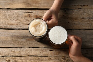 Friends with glass mugs of beer at wooden table, top view
