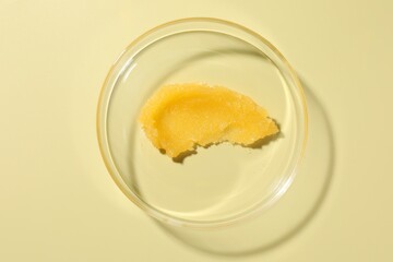 Cosmetic product in Petri dish on pale yellow background, top view