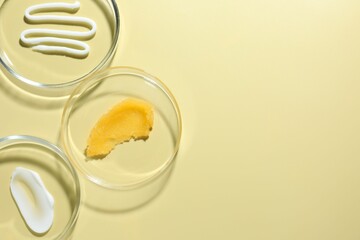 Different cosmetic products in Petri dishes on pale yellow background, flat lay. Space for text