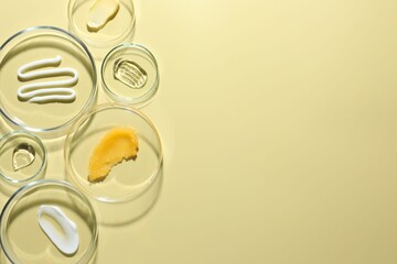 Different cosmetic products in Petri dishes on pale yellow background, flat lay. Space for text