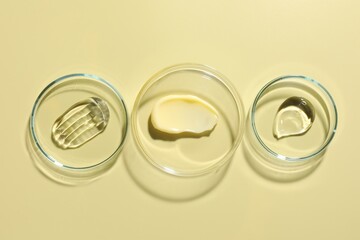 Different cosmetic products in Petri dishes on pale yellow background, flat lay