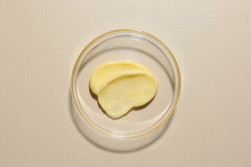Cosmetic product in Petri dish on beige background, top view