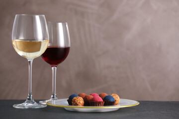 Delicious truffle bonbons and wine on black table against grey background. Space for text