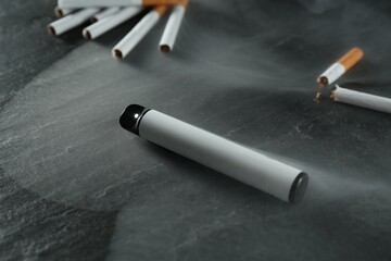 Electronic smoking device and cigarettes on black table, closeup