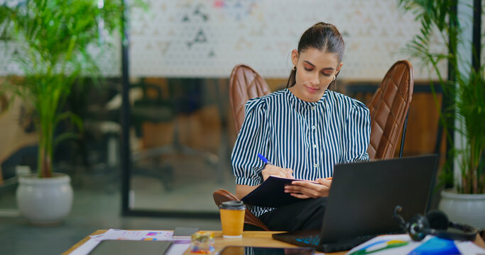 Indian gen z busy woman lady sitting chair use laptop on desk table look screen check email job office place young adult expert girl staff female do online work search day task data new idea plan