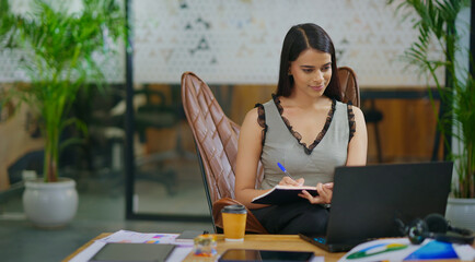 Indian gen z busy woman lady sitting chair use laptop on desk table look screen check email job...