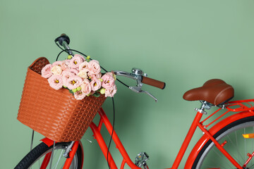 Bicycle with basket of beautiful flowers near light green wall indoors, closeup