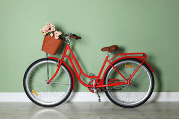 Bicycle with basket of beautiful flowers near light green wall indoors