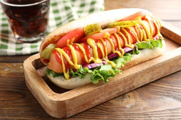 Tasty hot dog and soda drink on wooden table, closeup
