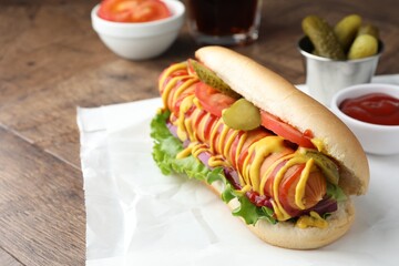 Tasty hot dog with vegetables, mustard and ketchup on wooden table, closeup. Space for text