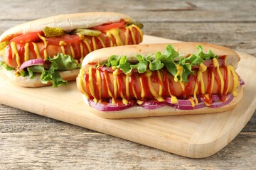 Tasty hot dogs with vegetables, mustard and ketchup on wooden table, closeup